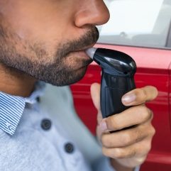 Homme utilisant un dispositif de test d'alcool au volant près d'une voiture.