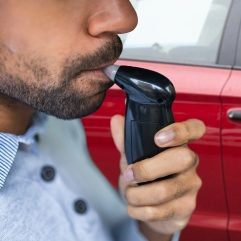 Homme utilisant un éthylotest près d'une voiture rouge.