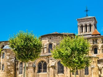 Église en pierre avec des arbres verdoyants sous un ciel bleu clair.