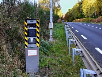Boîtier de radar de vitesse sur le bord d'une route, entouré de verdure.
