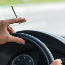 Conduite-sous-stupéfiants Main tenant un volant avec une cigarette entre les doigts.
