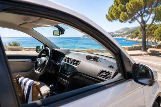 Vue de l'intérieur d'une voiture surplombant la mer et des arbres en bord de route.