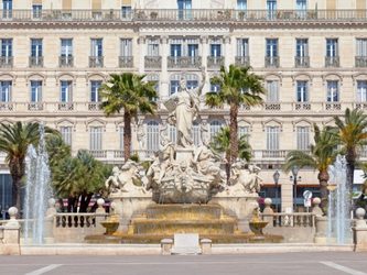 Fountain ornée de sculptures, entourée de palmiers, sur une place animée.